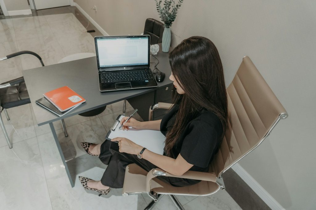 Woman working at a desk with a laptop and notebook.